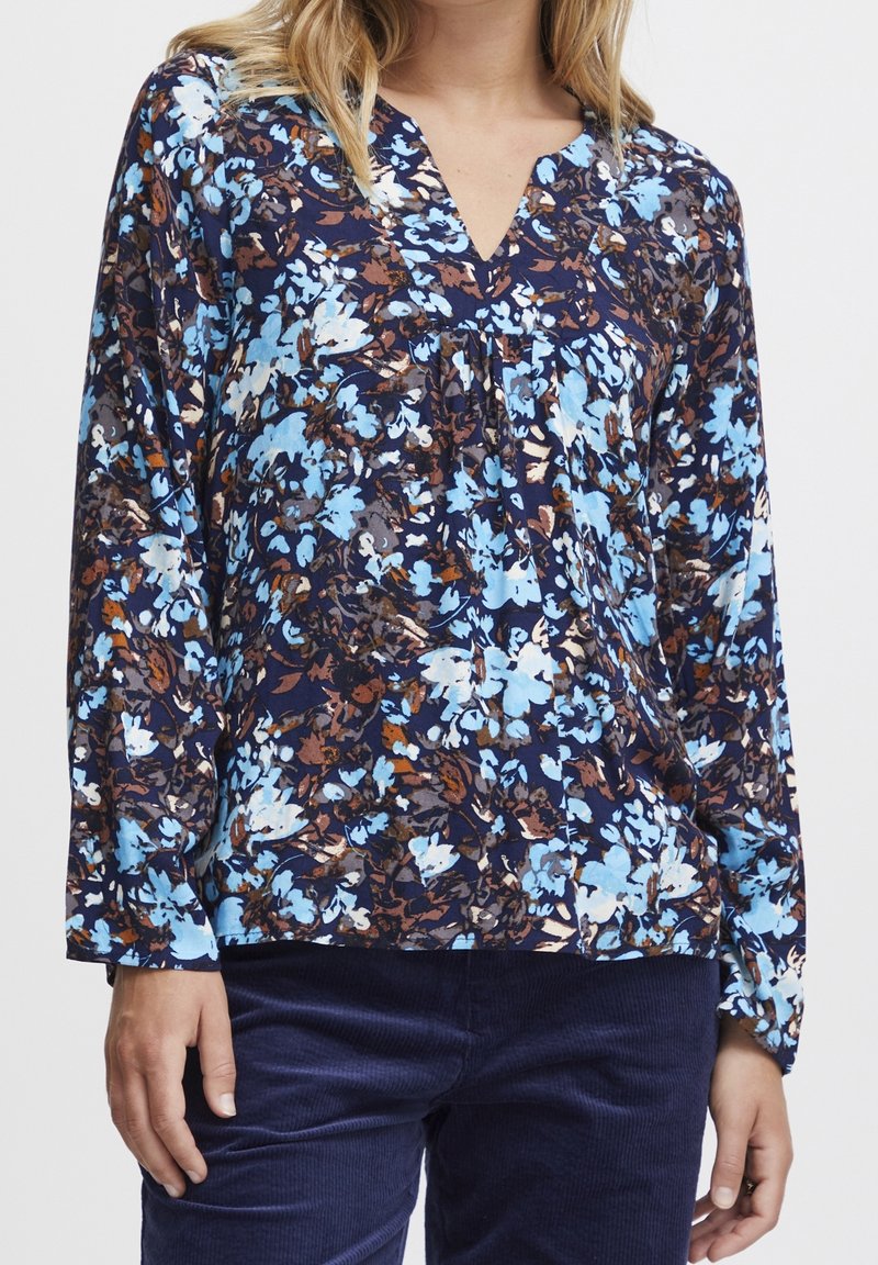 Blusa a maniche lunghe di colore blu navy con motivo floreale in azzurro chiaro e marrone, dotata di scollatura a V e dettagli arricciati sul petto.
