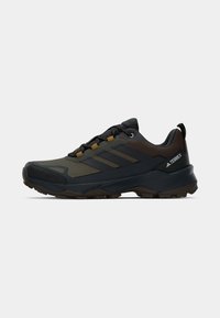 Scarpe da ginnastica verde scuro e nere con tessuto testurizzato, suola in gomma e contrasti marroni. Presentano tre strisce diagonali sui lati.