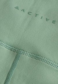 M一区 naslovna tkanina u mint zelenoj boji s teksturiranim završetkom. Sadrži “ACTIVE” logo i ravne šavove za izdržljivost. Glatki, rastezljivi materijal.