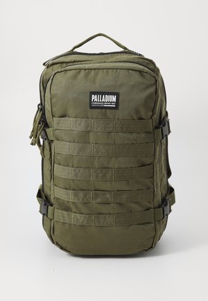 Sac à dos en nylon vert olive avec fermetures éclair, sangles en toile à l'avant, logo PALLADIUM et une poignée supérieure pour le transport. Dispose de sangles latérales réglables.