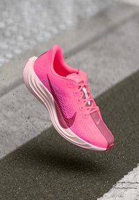 Vaaleanpunaiset juoksukengät, joissa on hengittävä verkko-osa ja pehmustettu pohja. Ominaisuuksia ovat gradienttimuotoilu ja erottuva Swoosh-logo sivussa.