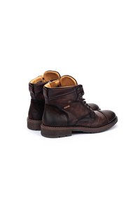 Botas de cuero marrón con un acabado suave, puntera redondeada y sistema de cordones. El interior está forrado en tela beige con acentos texturizados.