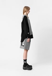 Sudadera oversized en negro y gris con un acabado texturizado, combinada con pantalones cortos grises. El modelo luce crocs negros, acentuados por calcetines con estampado.