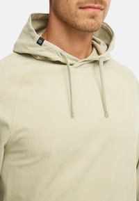 Lys grøn, ribbet stof hoodie med snoretræk, der har en hætte og et mærke i halsåbningen. Casual design med struktureret overflade.