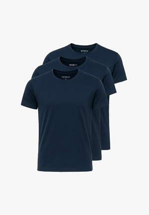 Marine crew-neck t-shirt parret med medium-wash blå jeans og hvide sneakers med brune detaljer. Model står med hænderne i lommerne.