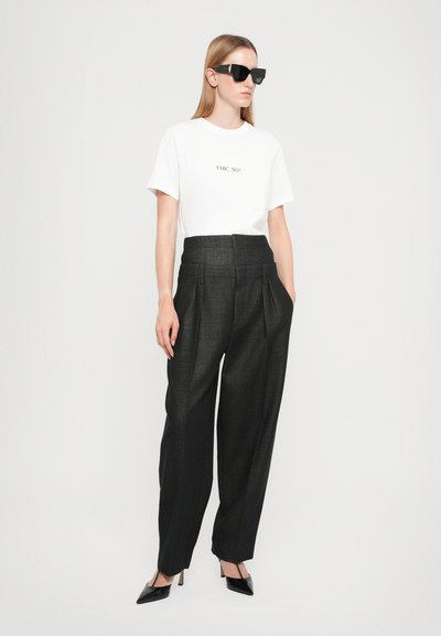 White t-shirt with "CHIC. NO?" printed. High-waisted black pleated trousers with a textured finish. Glossy black pointed-toe heels.