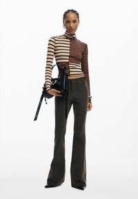 Pikkade varrukatega kõrge kaelusega top, beezide ja pruuni vertikaalsete triipudega. Oliivrohelised lõhikutega püksid detailse õmblusega, must käekott kõrvale.