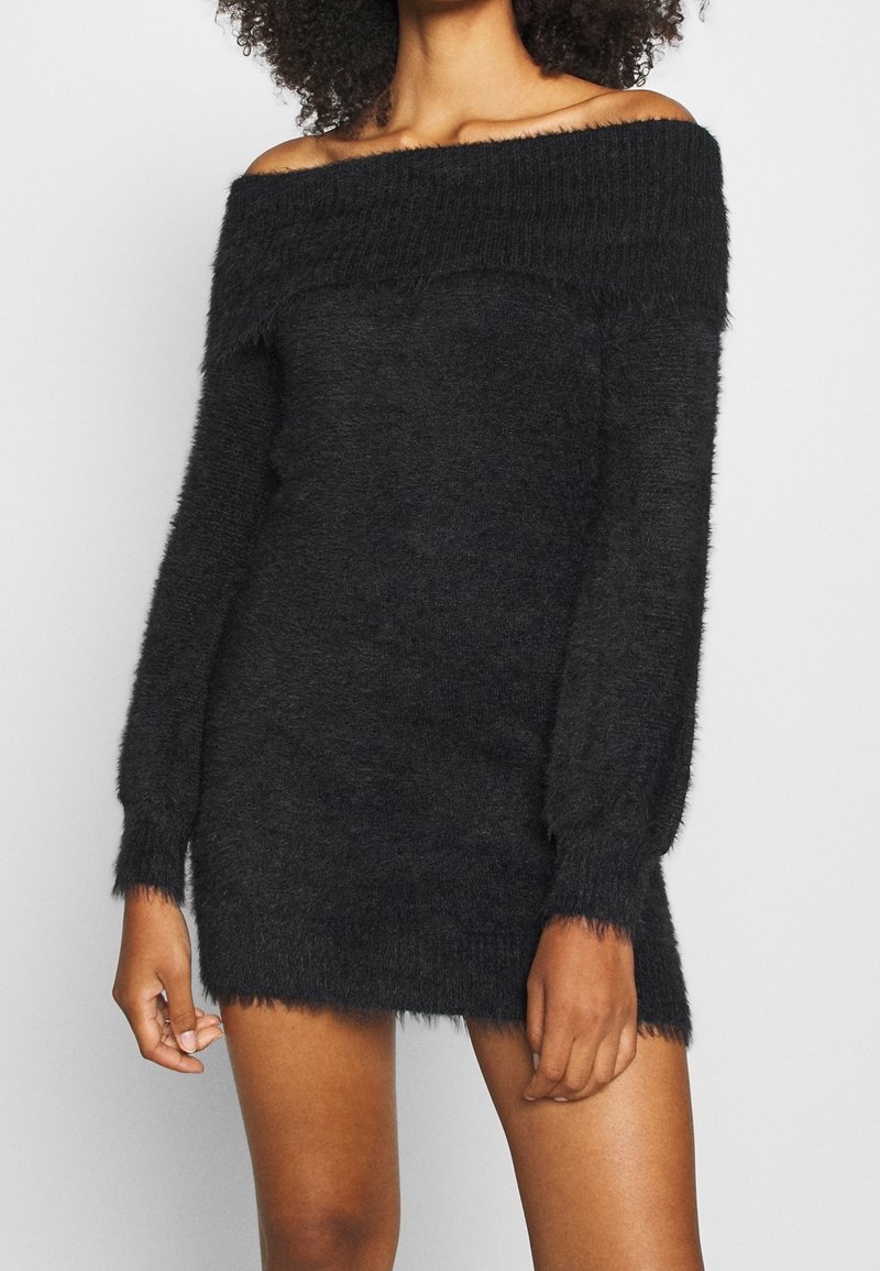 Robe-pull noire à épaules dénudées en tissu pelucheux, à manches longues et silhouette ajustée, avec un col et un ourlet côtelés.