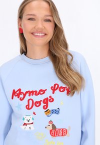 Jasnoniebieska bluza z haftowanymi kolorowymi psami z kreskówek oraz napisem "Mymo Pop Dogs" w kolorze czerwonym. Gładka tkanina, ściągacz przy dekolcie.