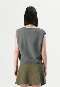 Person with straight dark hair wearing a sleeveless gray knit top and olive green skirt, shown from the back against a plain background.