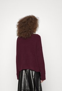 Överdimensionerad bourgognesweater i texturerad stickning, med en design med sänkt axel och ribbade manschetter, tillsammans med en svart läderskjorta.