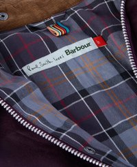 Bordowa kurtka od wewnątrz z szarym wzorem w kratę i pomarańczowymi oraz czerwonymi paskami. Zawiera metkę z napisem "Paul Smith loves Barbour." Widać szczegół z zamkiem błyskawicznym.