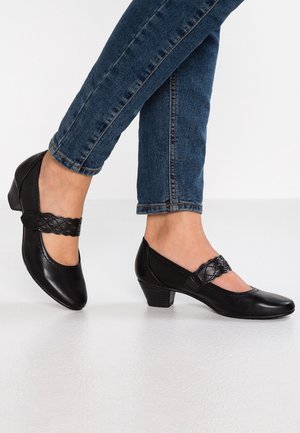Czarne skórzane buty na niskim obcasie z kwadratowym noskiem i ozdobnym plecionym paskiem, zestawione z dopasowanymi niebieskimi dżinsami. Gładka tekstura.