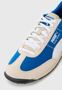 Sneaker in suede blu e beige con suola in gomma bianca, caratterizzati da una tomaia in rete, chiusura con lacci e marchio Puma. Design con punta arrotondata.