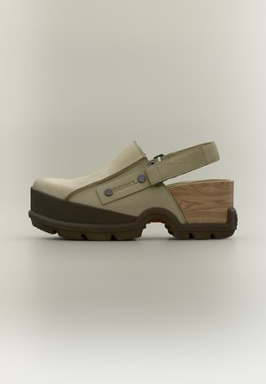 Sabots beiges avec semelle texturée marron foncé, talon bloc en bois, bride arrière réglable et logo SOREL sur le panneau latéral.