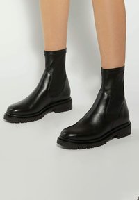 Black leather ankle boots with a smooth finish, elastic side panels, and a chunky treaded sole, featuring a low stacked heel.