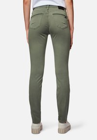 Jeans ajustados de color verde oliva con una textura suave, que presentan bolsillos traseros y sutiles detalles de costura, combinados con zapatillas blancas.