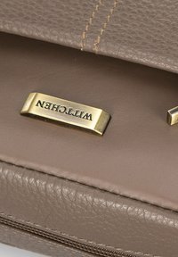 Kabelka z tanové kůže s texturovaným povrchem, s zlatým kováním a vyraženým logem. Viditelné švy dodávají designu detail.