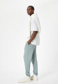 Avslappnad outfit med en vit t-shirt, ljus teal-joggingbyxor och vita sneakers. Joggingbyxorna har en mjuk textur och ett elastiskt mudd.