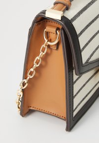 Sac en toile rayé avec des accents en cuir brun, détail en chaîne dorée et forme structurée ; il dispose d'une fermeture à fermeture éclair et d'une doublure intérieure contrastante.