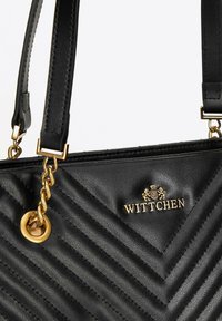 Borsa in pelle nera con texture a zigzag. Gli accessori in metallo dorato includono un logo e una catena. Presenta doppi manici per il trasporto.
