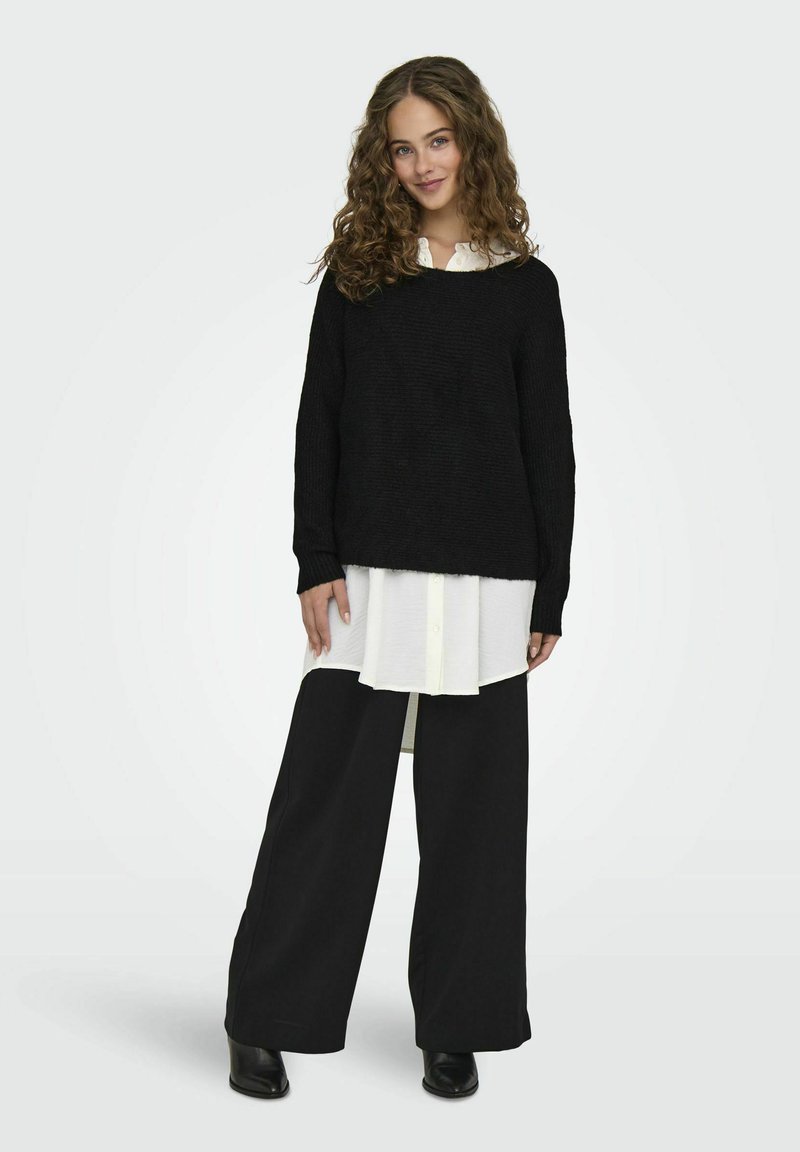 Black knitted sweater over a white button-up shirt, paired with wide black trousers and black ankle boots. Features long sleeves and textured fabric.