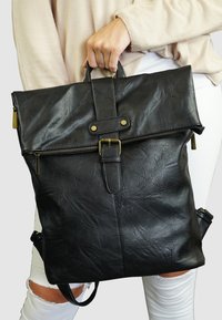 Zwarte faux leren backpack met verstelbare schouderbanden, een handvat aan de bovenkant, een voorzak met rits en een klep die is beveiligd met een gesp. Textuur op het oppervlak.