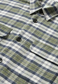 Camicia flanellata a quadri in verde, blu navy e bianco. Presenta bottoni neri, un colletto e due tasche sul petto realizzate in un tessuto textures.