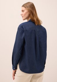 Mörk denimskjorta med långa ärmar, klassisk krage, ryggveck och uppvikta ärmslut. Har en slät textur och skräddarsydd passform.