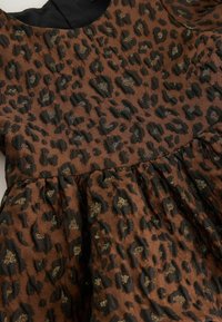 Leopárd mintás ruha barna és fekete anyagból, gyűrt szoknyával és arany díszítéssel a mintában.