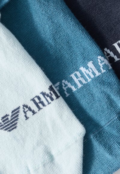 Τρία διπλωμένα πλεκτά κομμάτια σε λευκό, μπλε και ναυτικό μπλε με κείμενο ARM και λογότυπο με μοτίβο σε αντίθετα χρώματα κατά μήκος των άκρων.