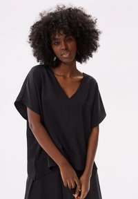 Zwart kortoeven T-shirt met een V-halsontwerp. Zachte stof, relaxed fit en een iets langere achterkant dragen bij aan de algehele silhouet.