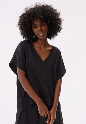 Schwarzes T-Shirt mit kurzen Ärmeln und V-Ausschnitt. Weicher Stoff, lockere Passform und ein leicht längerer Saum hinten ergänzen die Gesamtoptik.