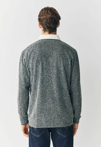 Grå houndstooth-mønstret sweater med lange ærmer og en hvid krave, fremstillet af et tekstureret stof, parret med mørkeblå jeans.