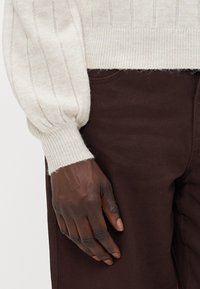 Maglione a coste di colore avorio con maniche a palloncino, caratterizzato da un lavorazione tessuta e polsini aderenti, abbinato a pantaloni marroni scuri.