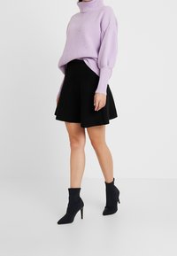 Lila gebreide turtleneck trui met oversized mouwen, gecombineerd met een zwarte flared rok en zwarte puntige hak enkellaarsjes.