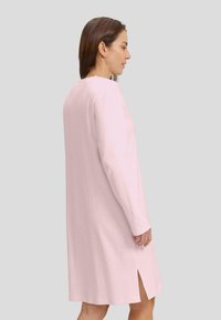 Vestido de manga larga en rosa claro con patrón de espiga, que presenta un escote redondo y aberturas laterales para facilitar el movimiento.