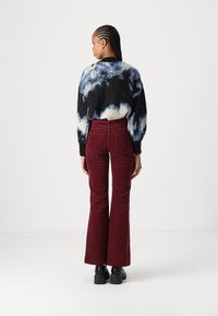 Svetr s černobílým barevným vzorem ve stylu tie-dye, volný střih, v kombinaci s vysokými bordovými manšestrovými kalhotami s rozšířenými nohavicemi. Černé boty na robustním podpatku.