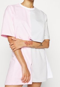 Růžové a bílé oversized tričko vyrobené z bavlny; má krátké rukávy, kulatý výstřih a logo Adidas na levé straně hrudi.