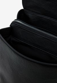 Innenraum einer schwarzen Lederhandtasche mit mehreren Fächern und einer Reißverschlusstasche. Weiche Textur mit glatter, matter Oberfläche.