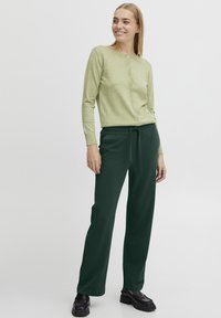 Light green, long-sleeve cardigan with button closure paired with dark green, loose-fit pants featuring a drawstring waistband. Black shoes.