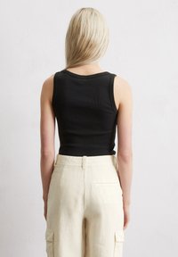 Schwarzes geripptes Tanktop mit rundem Ausschnitt, kombiniert mit beigen Cargo-Hosen mit Taschen und weitem Schnitt. Hintergrund ist rein weiß.