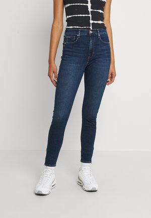 Jean skinny bleu foncé en denim, avec une taille haute, des coutures minimales et un design classique à cinq poches. Portez-le avec des baskets blanches.