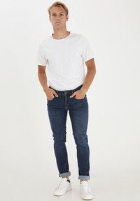 Fehér rövid ujjú póló, sötétkék slim-fit farmernadrág és fehér tornacipő. Egyszerű dizájn, könnyű textúra, a farmernadrágon pedig felhajtott ujjak.