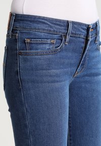 Džínové kalhoty v středně modré barvě s přiléhavým střihem. Vlastnosti zahrnují pět kapes, viditelné prošívání a hladkou texturu.