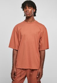 Tricou cu mânecă scurtă supradimensionat în culoarea teracotă, realizat din bumbac. Prezintă un gât în formă de cerc și o croială lejeră, cu cusături minime.