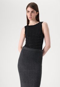 Top fără mâneci, de culoare neagră, cu un model de țepi argintii; asortat cu o fustă gri închis, cu nervuri, care are talie înaltă și o textură moale.