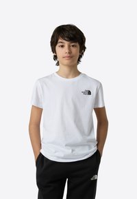 Tricou alb din bumbac cu guler rotund, având un logo negru pe pieptul stâng, asortat cu pantaloni negri cu un logo lângă buzunar.