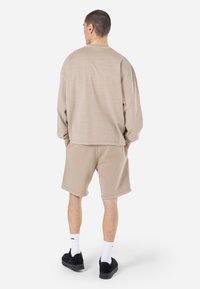 Beige színű, oversized kapucnis pulóver és azonos anyagú nadrág, puha textúrával. Könnyed, laza fazon, ejtett vállakkal és zsebes részletekkel.