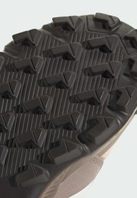 Gumeni đonovi sportskih cipela sa dubokim, uglatim žljebovima za prianjanje. Materijal je tamno smeđe boje sa teksturiranim žljebovima i razrezanim uzorcima.